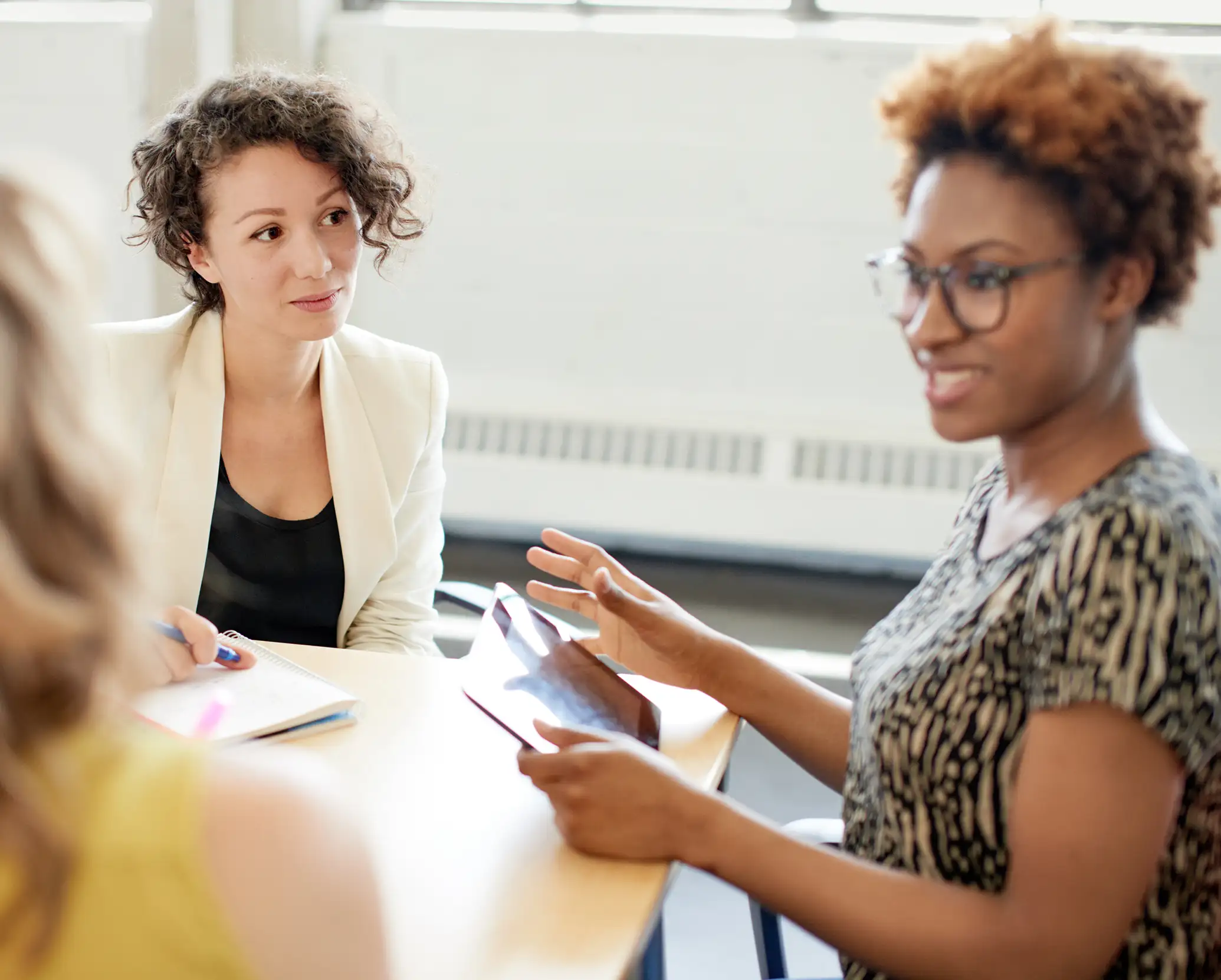Two women talking at a table, with one holding a tablet.