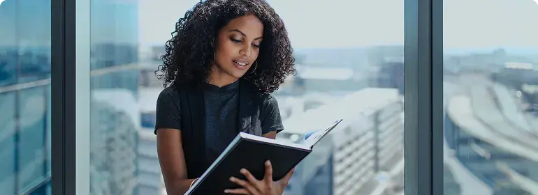 A woman reviewing documents beside an office window.