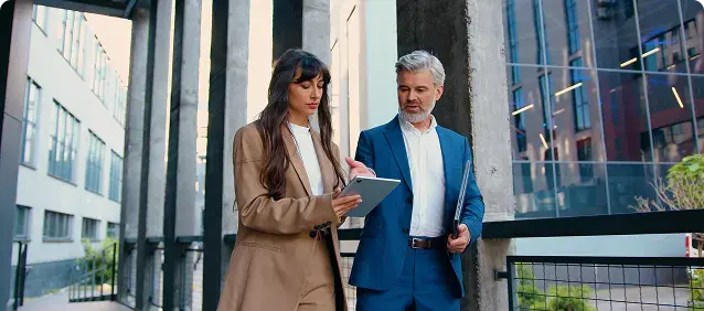 Two professionals discussing a tablet outside an office building.