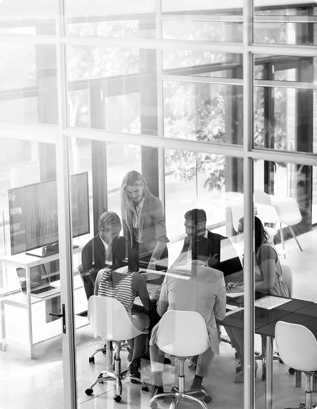 Colleagues gathered around a table in a glass-walled meeting room.