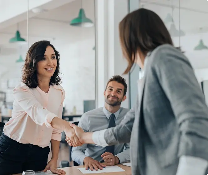 Two women shaking hands during an office meeting.