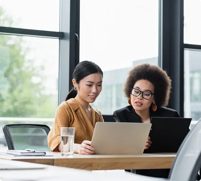 Two women reviewing information on a laptop at a table.