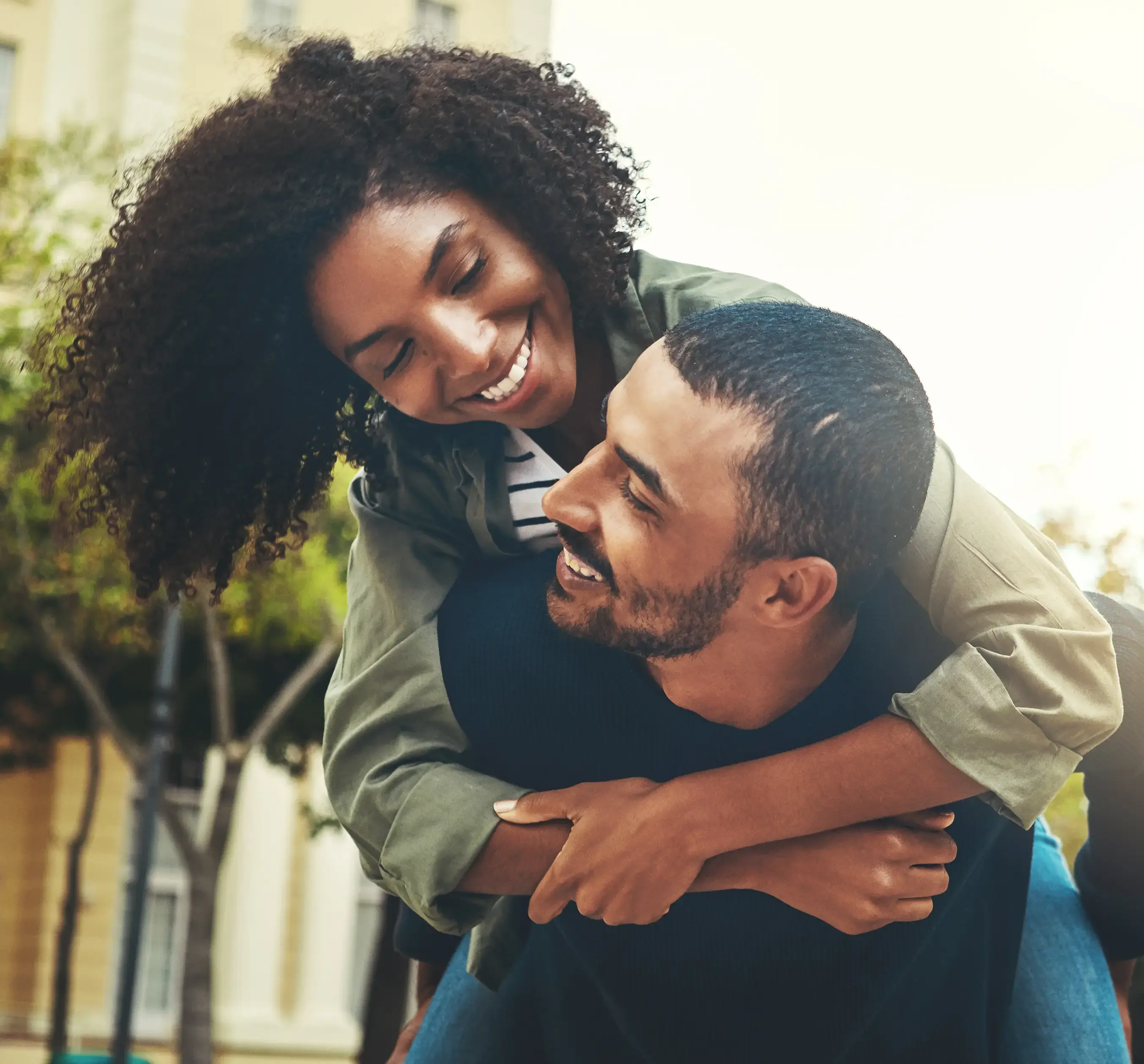 A smiling couple sharing a piggyback ride outdoors.